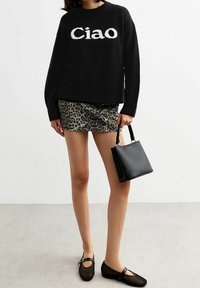 Schwarzer gestrickter Pullover mit "Ciao"-Text, kombiniert mit einem glänzenden Minirock im Leopardenmuster. Enthält eine kleine schwarze Handtasche und Mesh-Ballerinas.