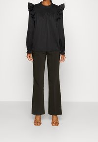 Blusa nera in cotone con maniche arricciate e scollatura smock, abbinata a pantaloni flare verde scuro e sandali marroni con cinturini.