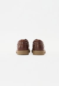 Pantofi din piele maronie cu un finisaj neted și lucios, având o formă rotundă și tălpi din cauciuc bej. Include accente laterale pentru detalii.
