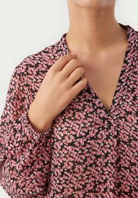 Langärmlige Bluse aus durchscheinendem schwarzen Stoff mit einem pink-weißen abstrakten Muster, ausgestattet mit einem V-Ausschnitt und elastischen Manschetten.