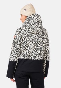 Kurtka w panterkę z czarną dolną częścią i kapturem, wykonana z teksturowanej tkaniny. Beżowa czapka dziana z wzorem w warkocze.