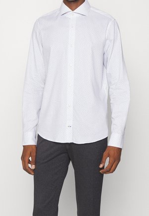 Man wearing a white long-sleeve button-up shirt with a subtle gray dot pattern and dark gray trousers.