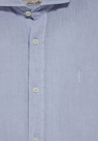 Jasnoniebieska lniana koszula o gładkiej fakturze, z guzikowym zapięciem z przodu oraz haftowanym logo postaci po lewej stronie.