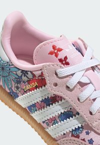 Zapatilla Adidas Samba con estampado floral rosa, confeccionada en materiales de ante y sintéticos, con rayas blancas, detalles en rosa y suela de goma texturizada.
