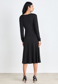 Black long-sleeve dress with a fitted bodice and flared skirt, made from smooth fabric; features a round neckline and sleek design.
