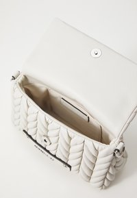 Borsa a tracolla in pelle bianca con design trapuntato, con hardware argentato e chiusura a scatto. L'interno è foderato con un tessuto uniforme. Forma compatta e strutturata.