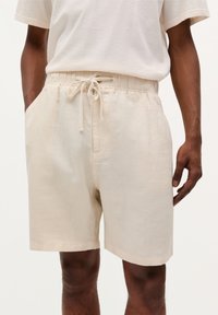 Beige shorts valmistettu liinasta, joissa on elastinen vyötärö ja nyöri, sivutaskut ja rento istuvuus. Niissä on sileä rakenne ja yksinkertainen muotoilu.
