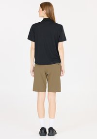Svart polotröja och khakishorts. Tröjan har en avslappnad passform; shortsen är knälånga med en dragkedjeficka. Svart fotränta och vita strumpor.