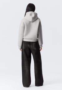 Grå hoodie med huva och ribbade ärmslut, tillsammans med vida svarta denimbyxor med ett subtilt mönster på benen.