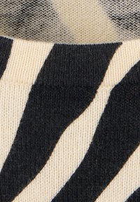 Gros plan d'un tissu tricoté noir et beige avec un motif rayé audacieux et irrégulier et des détails de couture visibles.