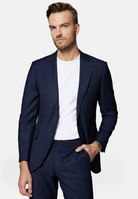 Granatowy garnitur w kratę z dopasowaną marynarką i pasującymi spodniami, połączony z białym t-shirtem z okrągłym dekoltem. Teksturowany materiał i dopasowany krój.