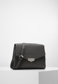 Borsa a tracolla in pelle nera con chiusura a patta, ferrature in argento e tracolla regolabile. Texture liscia con dettagli di cuciture visibili.