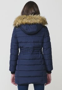 Giacca puffer blu navy con cappuccio staccabile bordato di pelliccia, design a trapunta e polsini a coste, dotata di vita aderente e lunghezza media.
