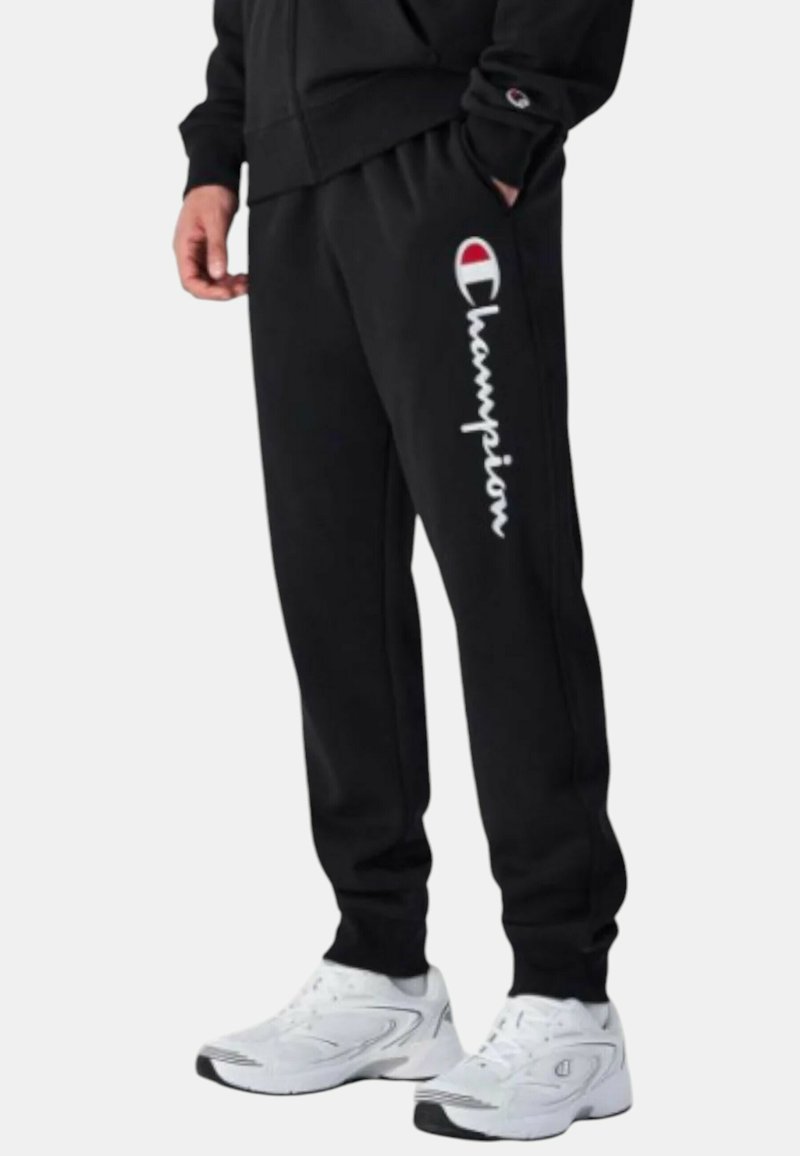 Pantaloni da jogging neri realizzati in tessuto misto cotone, con logo "Champion" bianco e un emblema sulla coscia sinistra. Rifiniti con polsini elastici.