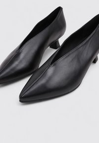 Zapatos de cuero negro con punta afilada, tacón bajo y diseño cortado en la parte superior. Textura suave y detalles de costura mínimos.