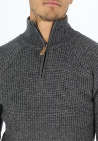 Pullover grigio a coste con collo alto e chiusura a zip a metà. Presenta cuciture a contrasto e un piccolo tag in pelle sulla cerniera.