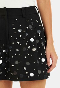 Gonna nera con paillettes circolari e strass di diverse dimensioni, con pieghe e una texture di tessuto liscia.