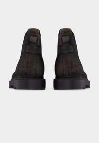 Ζευγάρι σκούρων καφέ δερμάτινων μποτάκια αστραγάλου με παχιές μαύρες σόλες, προβολή από πίσω, με δερμάτινες ετικέτες με το εμπορικό σήμα.