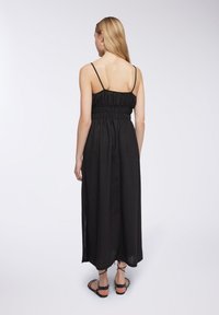 Abito maxi nero senza maniche con vita arricciata, orlo dritto e tessuto traspirante. Indossato con sandali piatti e con cinghie.