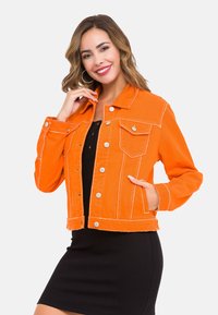 Orangenes Jeansjackett mit kontrastierenden weißen Nähten, Fronttaschen und Druckknöpfen. Über einem schwarzen Kleid getragen.