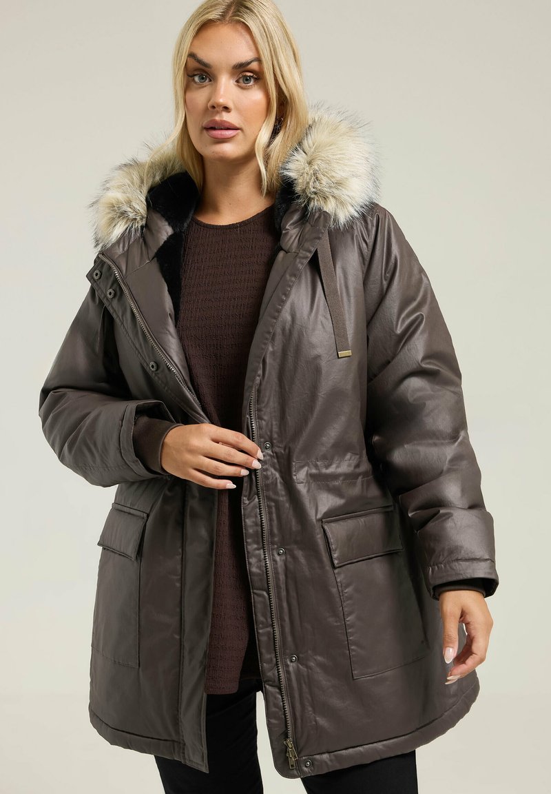 Parka matelassée marron foncé avec capuche en fausse fourrure, fermeture éclair et boutons-pression, grandes poches avant et texture lisse et brillante.