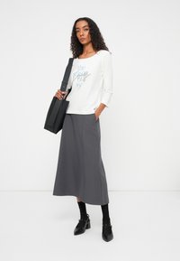 White long-sleeve shirt with blue text, paired with a gray maxi skirt. Black shoulder bag and shoes complete the outfit.