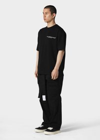 Sort oversized t-shirt med korte ærmer og logo på venstre bryst, parret med sorte cargo-bukser med lommer og et label.