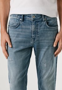 Jeans de mezclilla azul claro con un corte recto, que presentan un desvanecimiento sutil y un ligero desgastado en la parte delantera. Diseño clásico de cinco bolsillos con herrajes de metal.