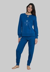 Completo loungewear blu composto da una maglia a maniche lunghe con grafica di un orso e un dettaglio a chiave, abbinato a pantaloni della tuta coordinati. Texture liscia.