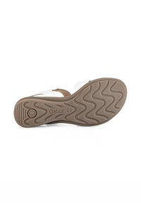 White sandal with brown rubber sole, featuring a textured zigzag pattern, brand logo, and adjustable straps for fit.