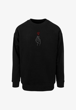 Mustarist sweatshirt, mille ees on valge kontuur käest, mis teeb südame žesti, ning selle kohal väike punane süda. Pehme tekstuur, mugav lõige.