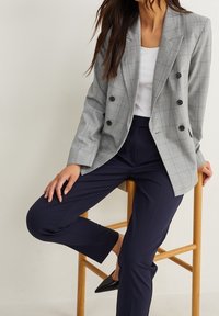 Blazer de cuadros gris de doble botonadura, confeccionado en una tela ligera, combinado con pantalones navy de corte ajustado y tacones negros de punta.