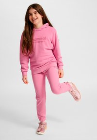 Rosa Hoodie- und Hosen-Set aus weichem Stoff, mit Logo auf dem Hoodie, bundgesäumten Hosen und glänzenden rosa Sneakers.