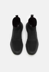 Black knitted ankle boots with a flexible upper and textured panels. Features a pull tab and a durable rubber sole, minimalist design.