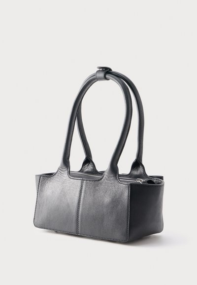 Μαύρη τσάντα χειρός από δέρμα με μακριές διπλές λαβές και κλείσιμο με φερμουάρ, εμφανίζεται μπροστά σε απλό ανοιχτό φόντο.