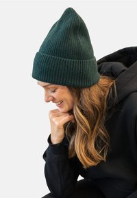 Zielona, prążkowana czapka beanie z zaostrzonym wierzchołkiem i podwiniętym mankietem. Miękki materiał z mieszanki wełny doskonale współgra z czarną bluzą w casualowym stylu.