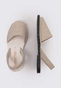 Sandalias de cuero beige con la parte trasera abierta, punta redondeada y suela de goma negra. Presentan costuras mínimas y una textura suave.