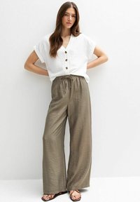 Haut blanc à manches courtes avec boutons associé à un pantalon large et décontracté en olive vert avec taille à cordon et texture subtile.