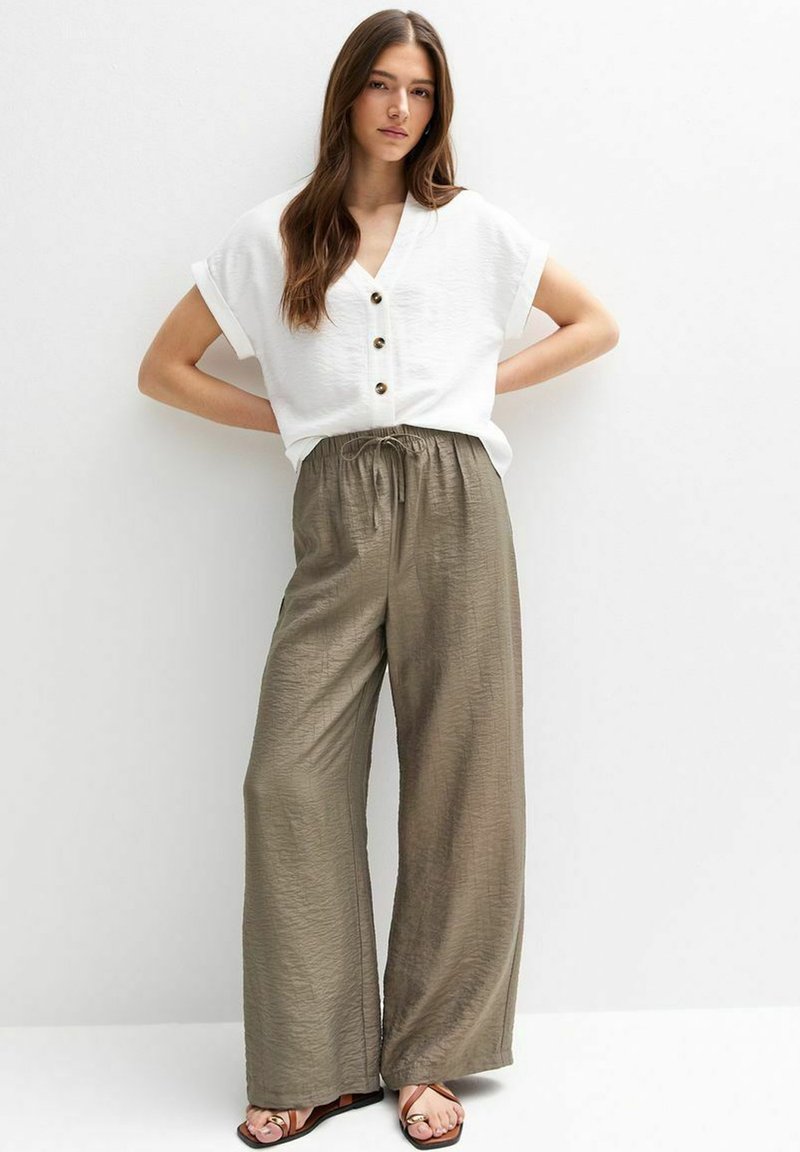 Haut blanc à manches courtes avec boutons associé à un pantalon large et décontracté en olive vert avec taille à cordon et texture subtile.