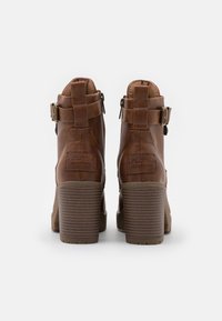 Paire de bottines en cuir marron avec talons blocs empilés, fermetures éclair latérales et sangles à boucles, vues de dos sur un fond blanc.