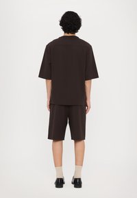 Brown short-sleeve shirt with a relaxed fit, paired with matching knee-length shorts, smooth texture, and minimal design details.