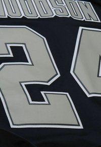 Schwarzes Sporttrikot mit großem grauen "22" in weißer Stickerei und Umrandung. Der Text ist in einer auffälligen, sportlichen Schriftart deutlich sichtbar.