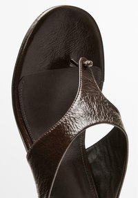 Dark brown leather sandal with a textured upper, a thong design, and a smooth footbed. Features a minimalistic style and secure fit.
