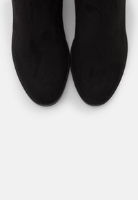 Sorte ruskind ankelstøvler med spids tå og minimale syninger. Designet har en glat tekstur og en slank, strømlinet silhuet.