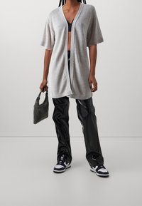 Ljusgrå oversized cardigan med V-hals, korta ärmar, öppen front, i kombination med glänsande svarta vida byxor och en strukturerad svart handväska.