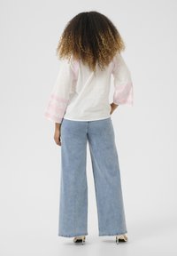 Camicia bianca con accenti ricamati rosa sulle maniche, abbinata a jeans a gamba larga azzurri. Tessuto testurizzato e maniche svasate.