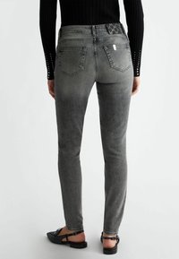 Jeans de mezclilla gris ajustados con una cintura de altura media, bolsillos traseros y un diseño cosido en la cinturilla. Superficie texturizada, con mínimo desgastado.