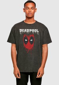 Juodas per didelis marškinėlis, pagamintas iš medvilnės, su nusidėvėjusiu Deadpool grafiniu dizainu raudonos ir juodos spalvų su lašėjimo efektais.