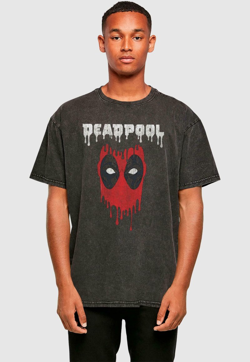 Juodas per didelis marškinėlis, pagamintas iš medvilnės, su nusidėvėjusiu Deadpool grafiniu dizainu raudonos ir juodos spalvų su lašėjimo efektais.