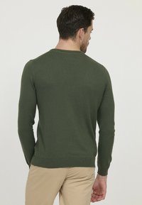 Pull en tricot vert avec un col rond, des manches longues et des poignets et un ourlet côtelés. Texture lisse, silhouette ajustée, design uni.